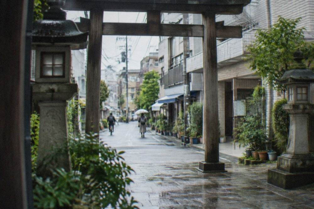 A wooden torii gate and stone lanterns along a quiet lane in Hakata