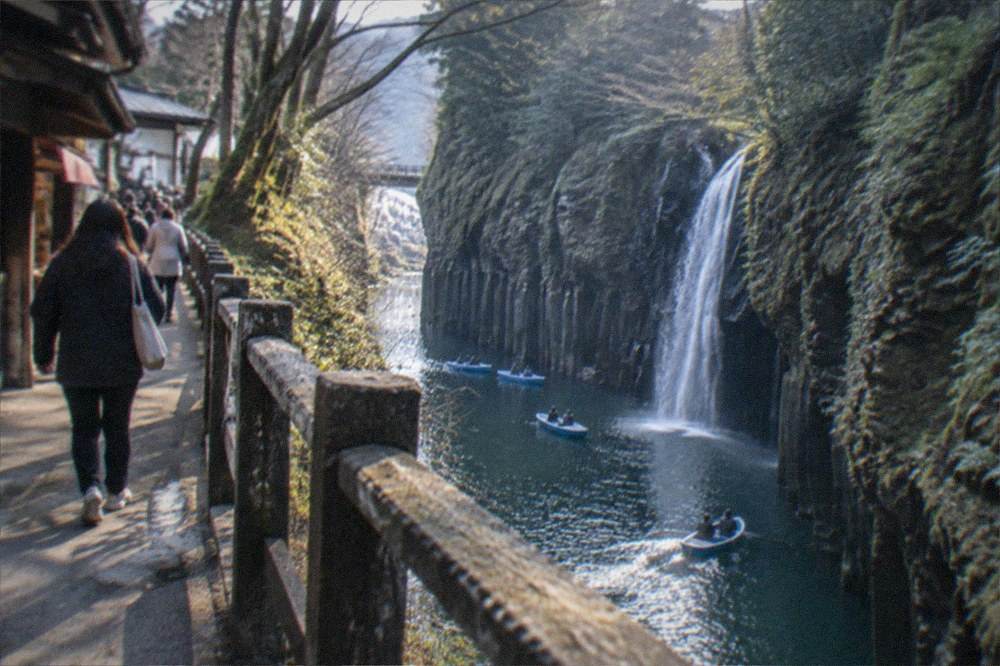 Takachiho Gorge with sheer cliffs and a boat on the water below a shrine town