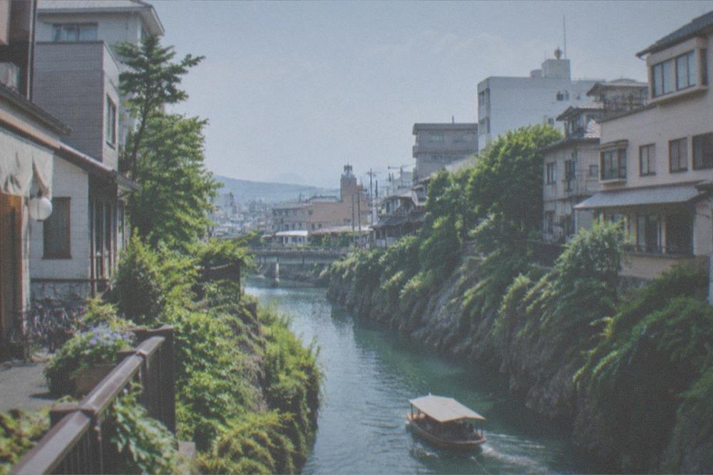 A narrow green gorge with a boat on turquoise water below tall cliffs
