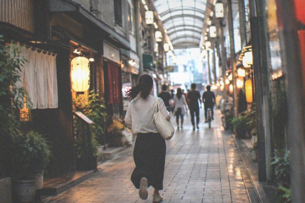 A narrow covered shopping arcade at night with small lit shopfronts and lanterns