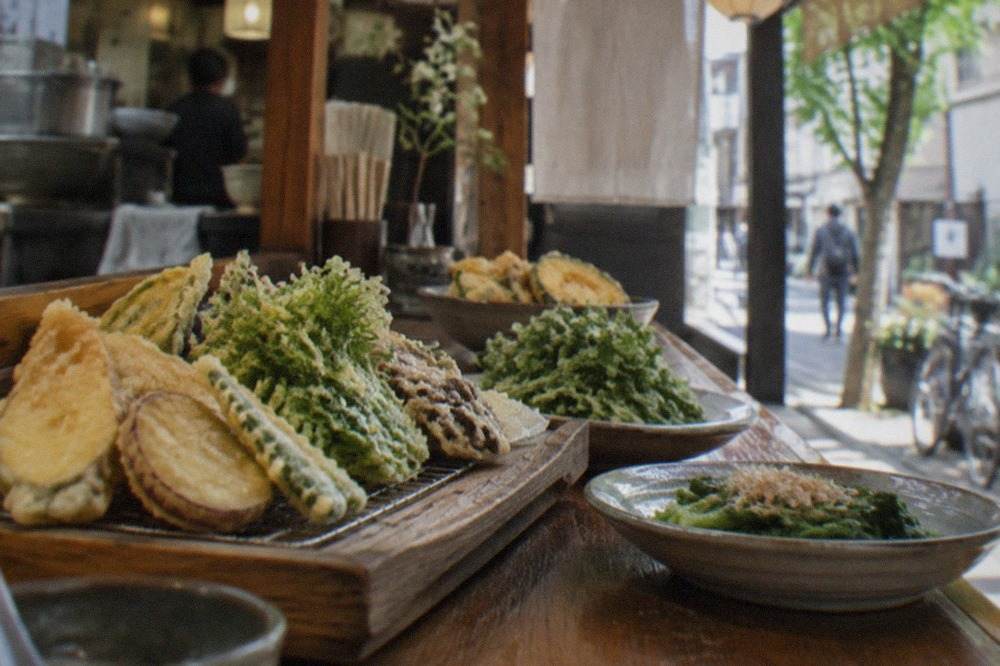 Fresh vegetable tempura and greens arranged on a wooden counter in a small Fukuoka restaurant
