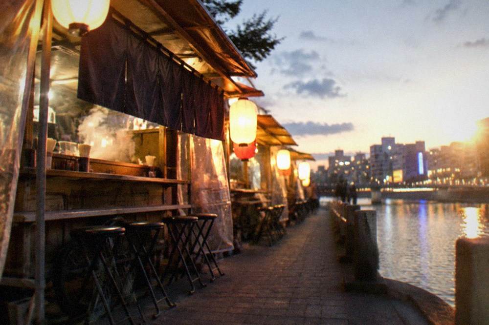 Illuminated yatai food stalls lined along a riverside street at night