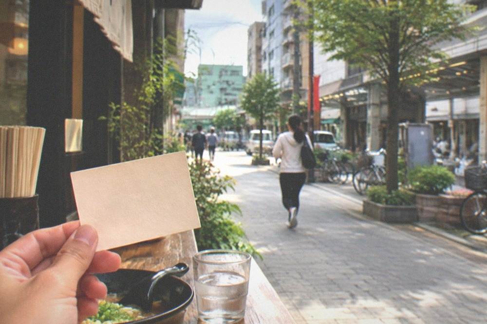 A small card with Japanese phrases held above a restaurant counter menu