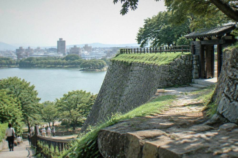 Stone walls of Fukuoka Castle ruins overlooking Ohori Park lake and the city skyline beyond