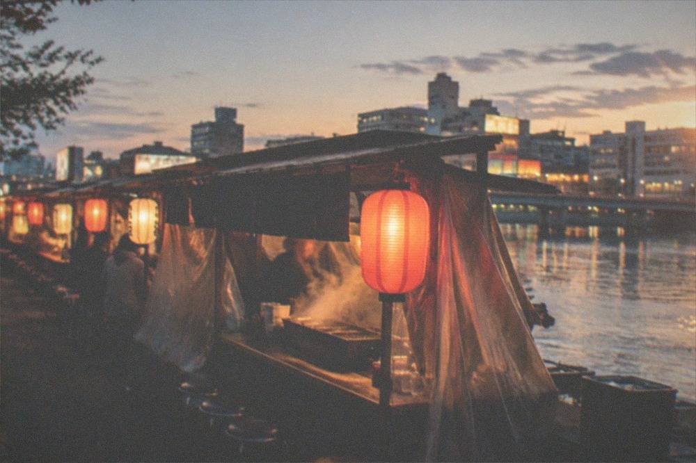 Row of lantern-lit yatai food stalls beside a river at night
