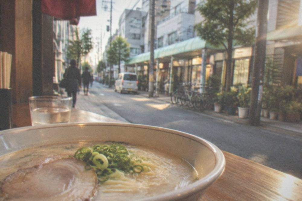 Bowl of creamy white tonkotsu ramen with thin noodles, chashu pork and green onion on a wooden counter