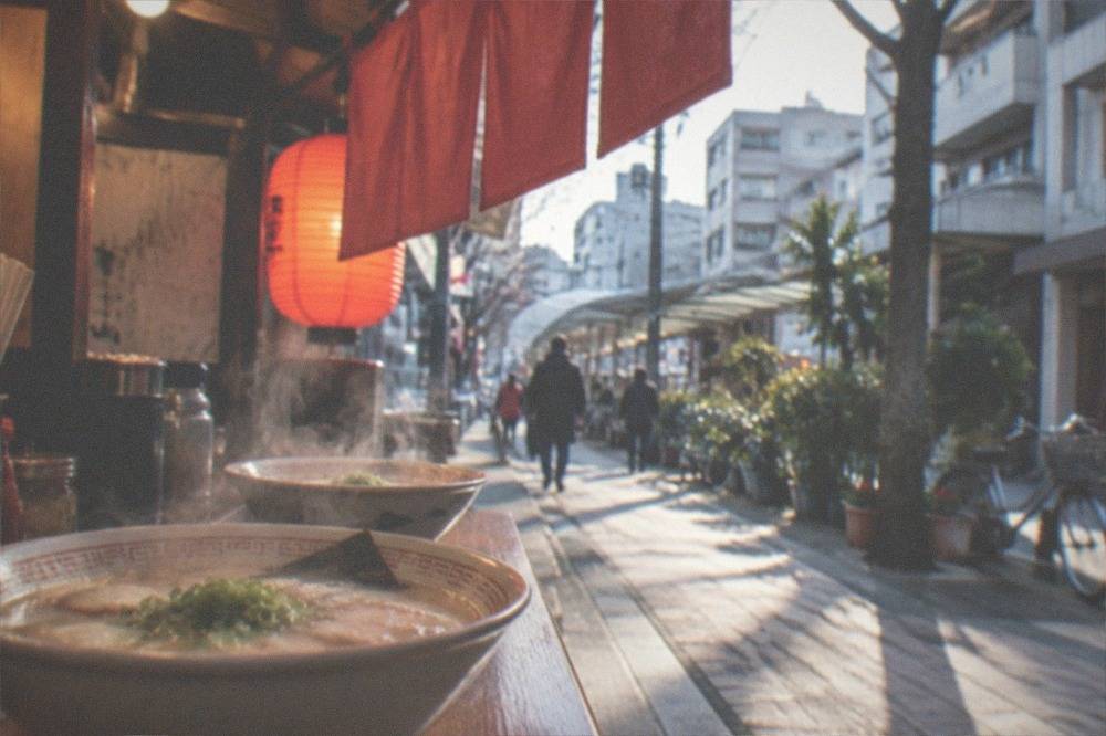 Steaming bowls of tonkotsu ramen on a wooden food stall counter under warm lantern light