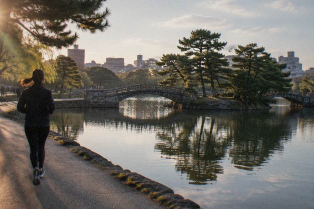 The calm water of Ohori Park lake with the stone bridge and pine trees reflected in the surface