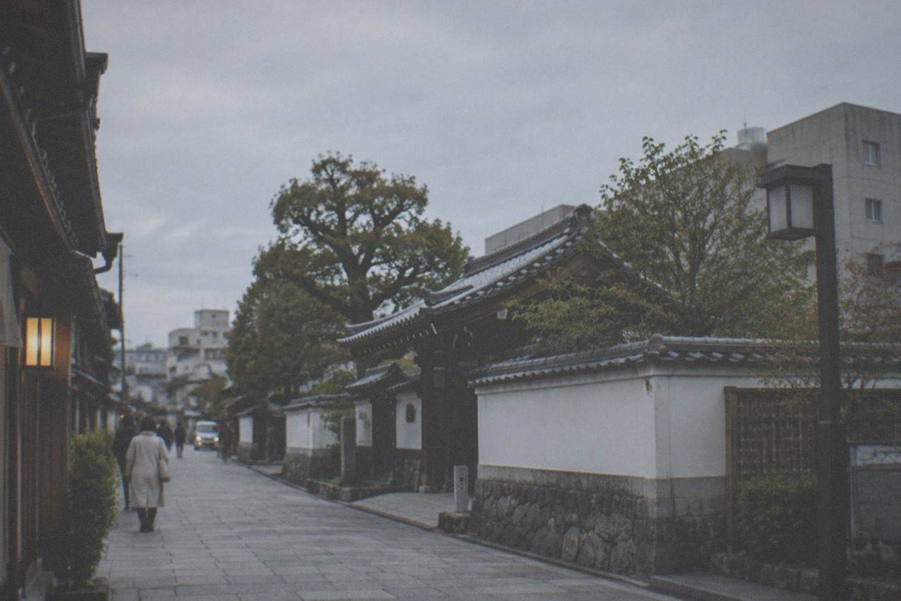 A quiet stone-paved lane in Hakata old town with traditional wooden machiya facades under a soft evening sky