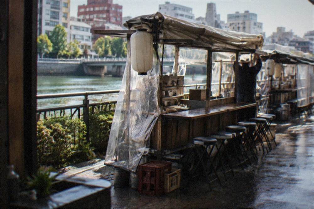 Food stall being packed up with its canvas roof folded and lanterns extinguished on a wet street