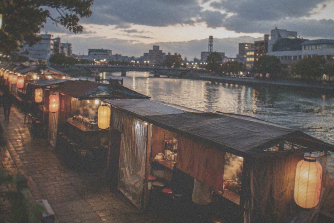 Row of lantern-lit yatai food stalls along a river embankment at night