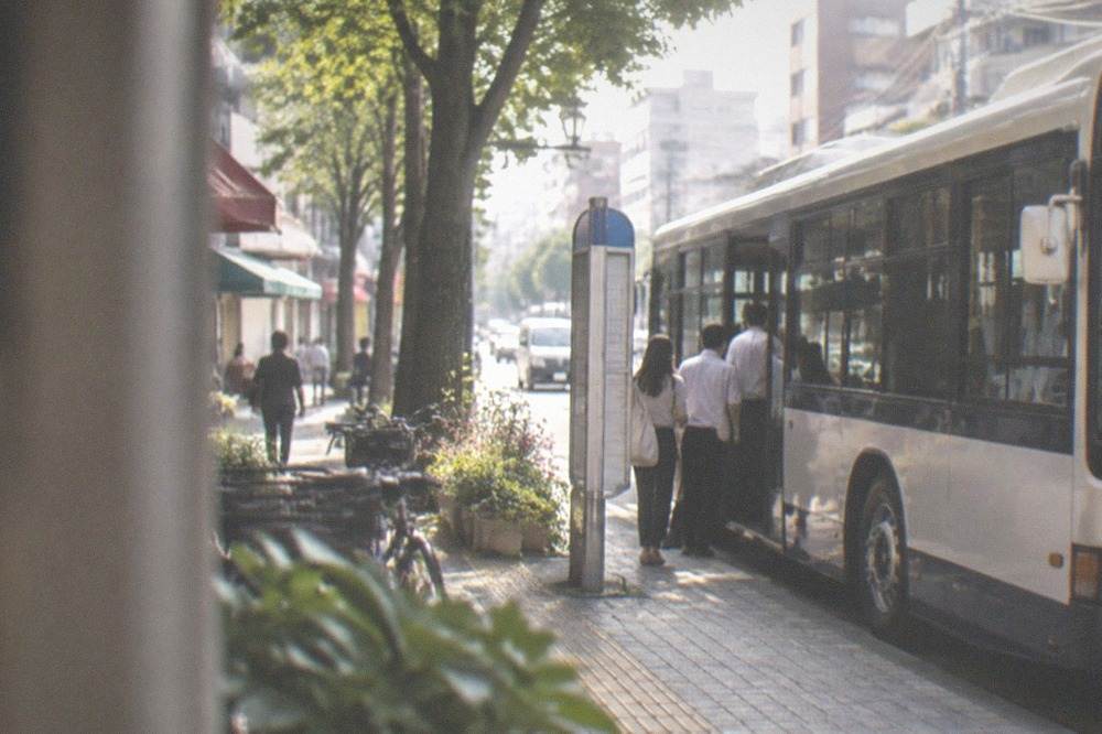 A city bus at a stop on a Fukuoka street with passengers boarding