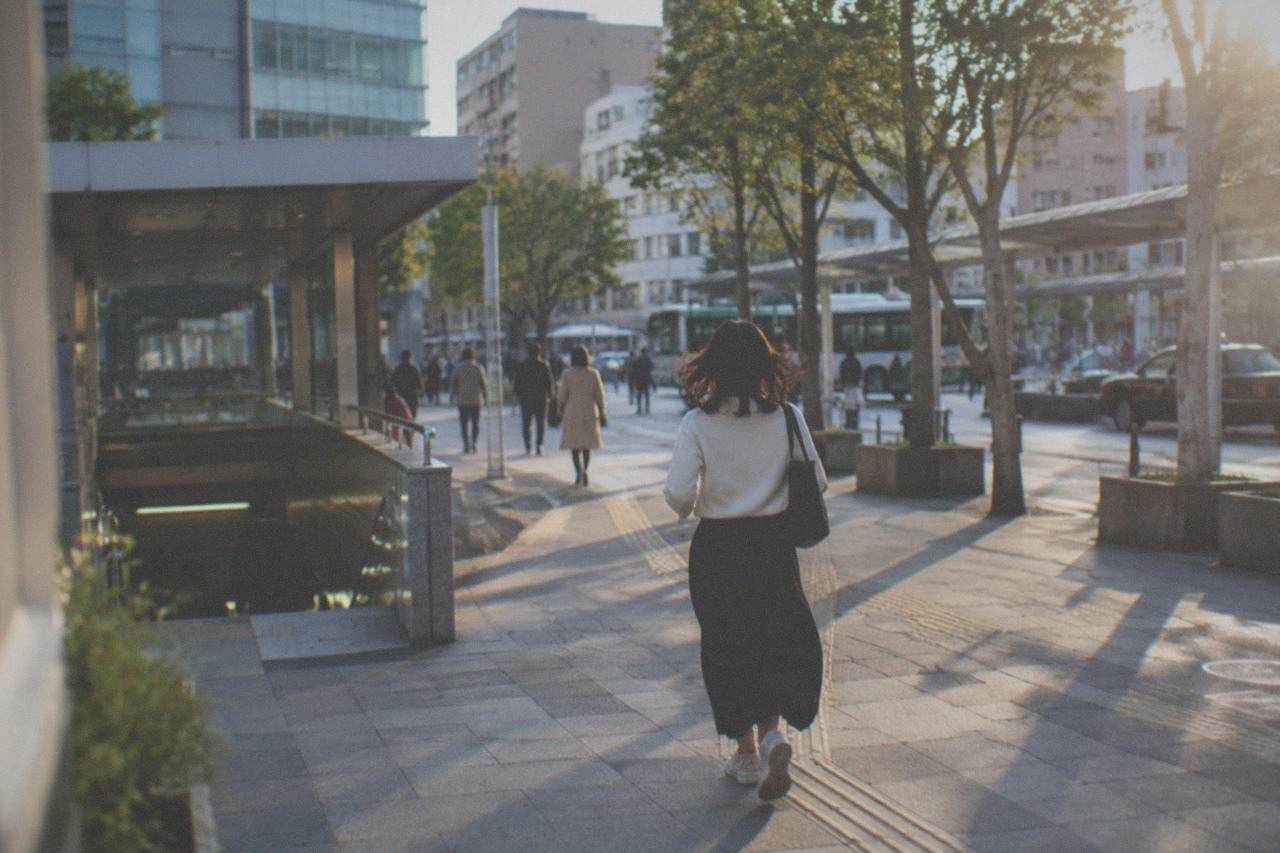 A Fukuoka city street with a subway station entrance and pedestrians on a wide sidewalk