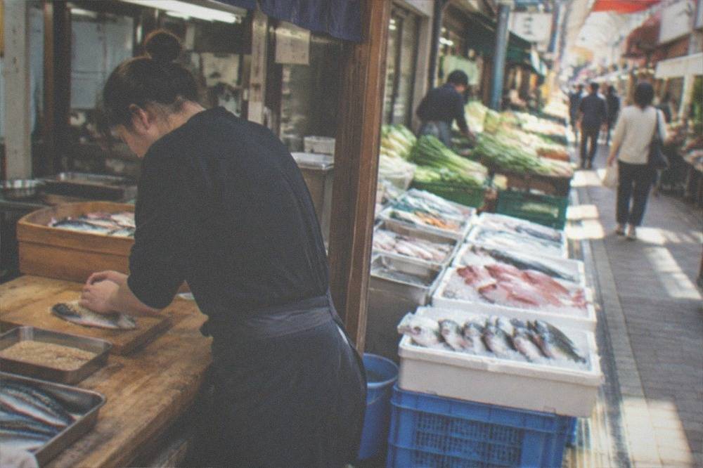 a cook pressing sesame seeds onto a slice of mackerel at a wooden counter