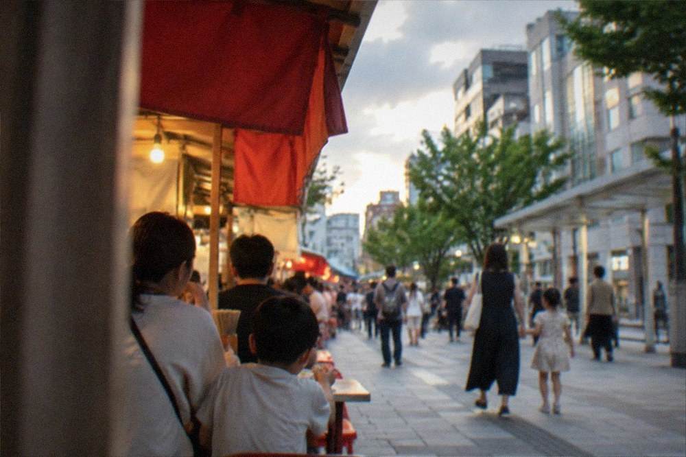 Families with children eating at street food stalls beside a festival route in the evening