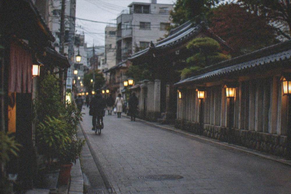 A quiet temple street in Hakata at dusk with lanterns glowing along the wall