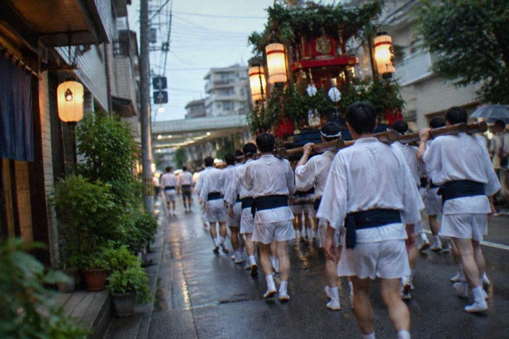 Team of men in traditional dress carrying a festival float down a narrow street at night