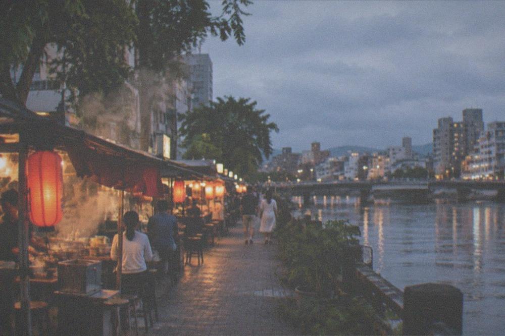 Steam rising from food stalls along a riverside street at night