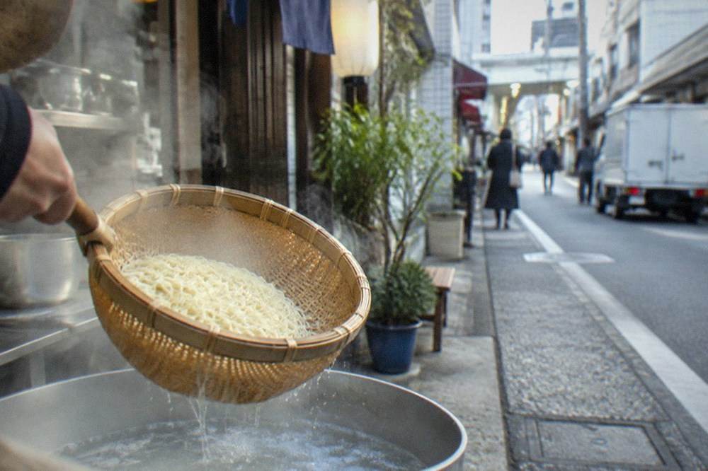 Fresh thin ramen noodles held in a bamboo basket over boiling water