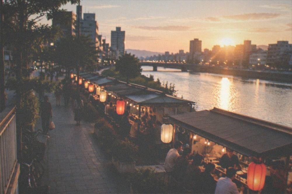 A row of illuminated food stalls along the river at night with customers seated at counters