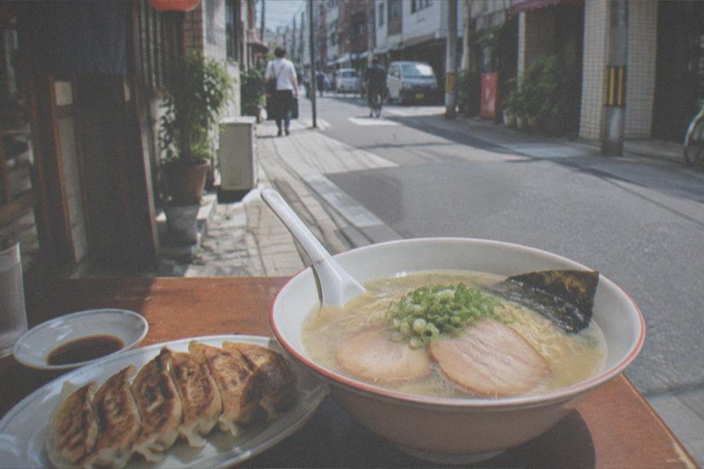 Small pan fried gyoza dumplings on a plate beside a bowl of ramen