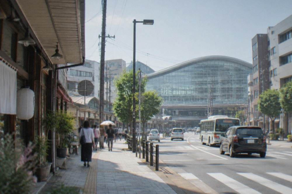 The curved glass facade of a large railway station building in Fukuoka under a clear sky