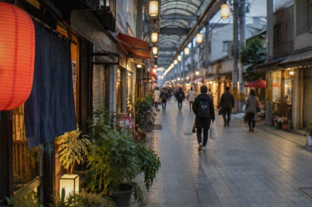 A lantern-lit shopping arcade at dusk with small shops glowing along its length