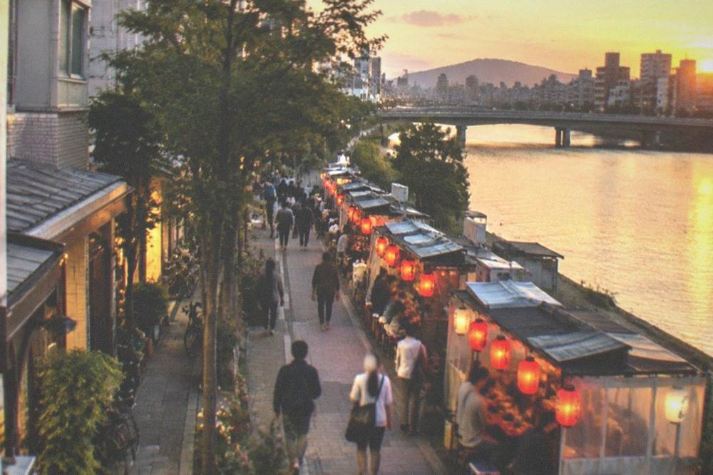 Food stalls with red lanterns glowing along a riverside street at night