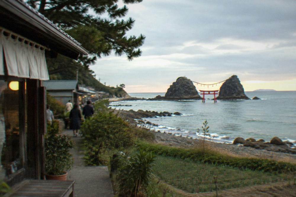 Two sea stacks joined by a rope with a red torii gate standing in shallow water at sunset