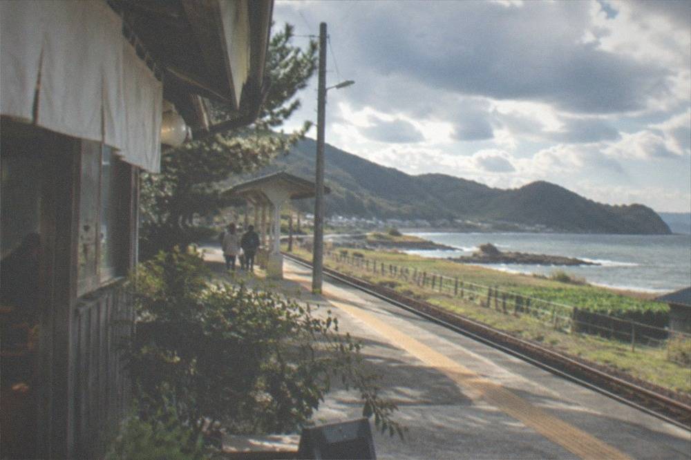 A small train station platform beside fields and low hills near the coast