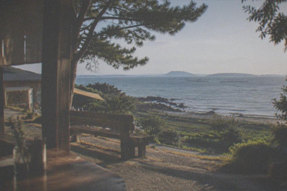 A wooden bench overlooking calm sea with oyster farming rafts on the horizon