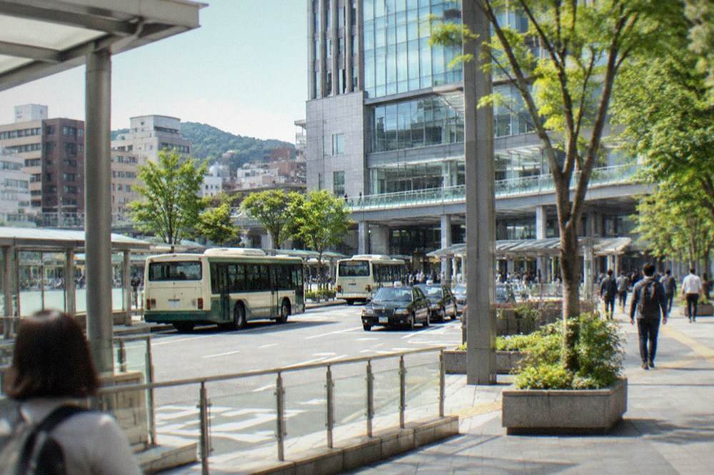 A green and cream sightseeing train standing in a rural Kyushu station surrounded by hills