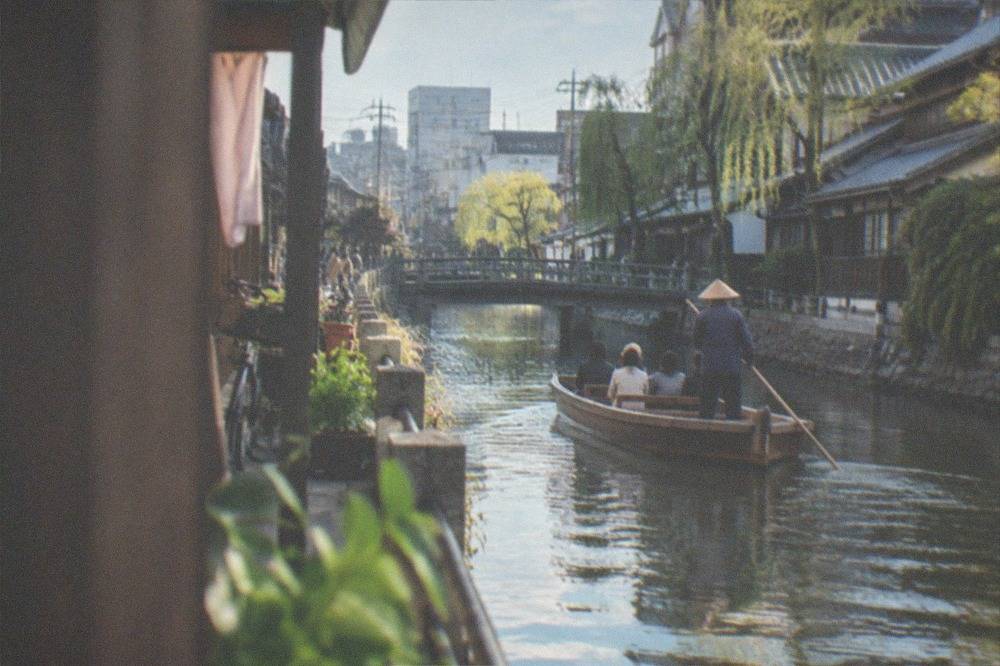 A canal boat being poled along a waterway in a small Japanese town lined with traditional buildings