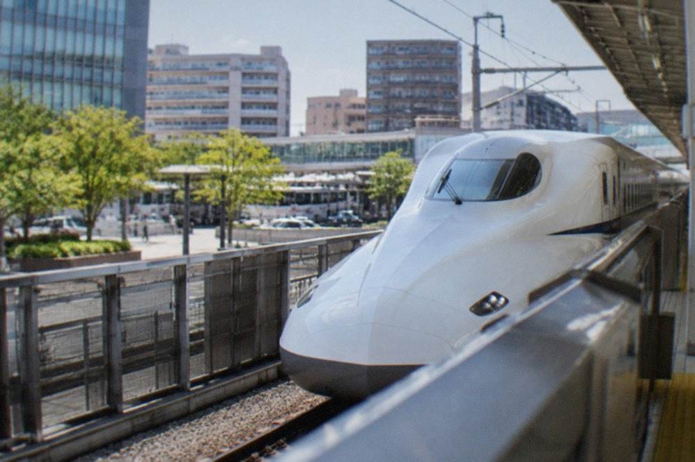 A white shinkansen bullet train waiting at a station platform under a bright sky