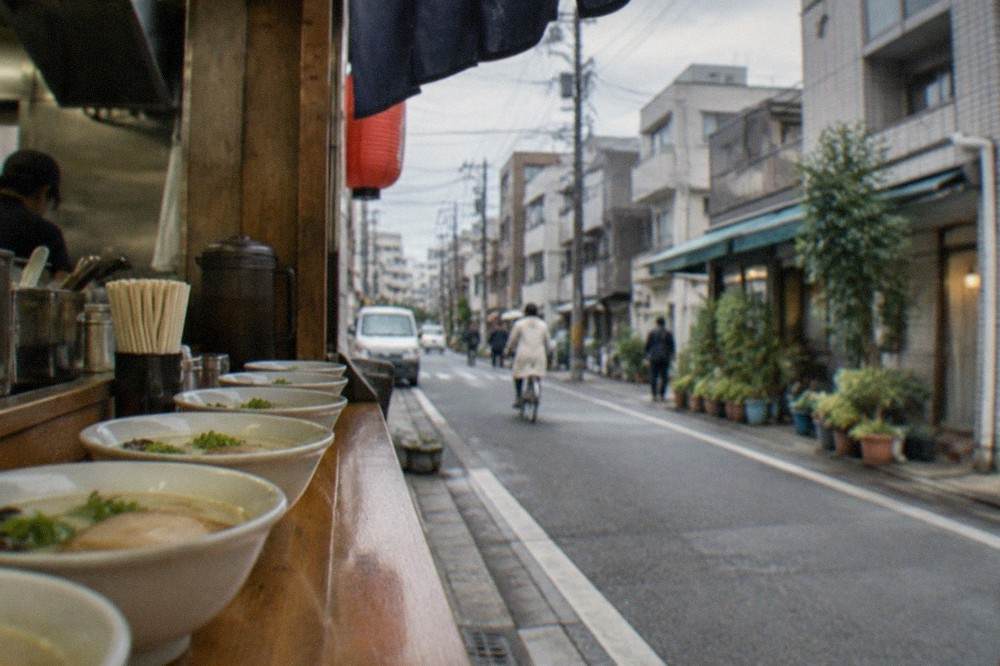 A row of white tonkotsu broth bowls lined up on a ramen shop counter with chopsticks and ladles