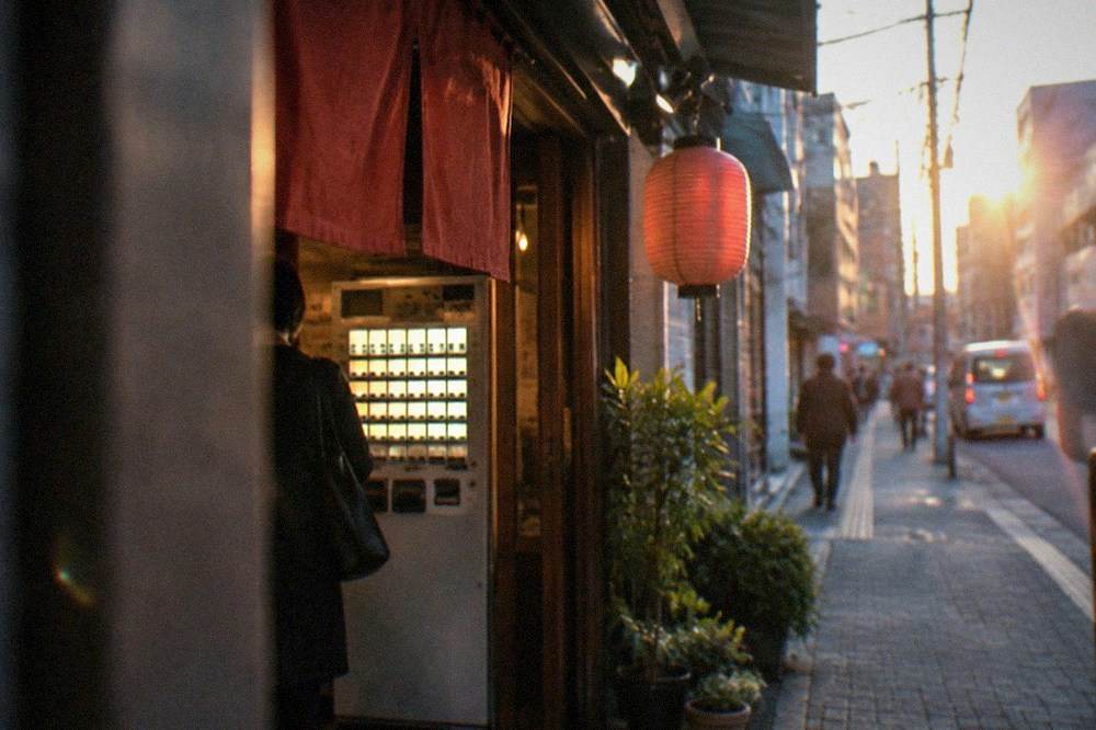 A ramen ticket machine with illuminated buttons beside a shop entrance at dusk