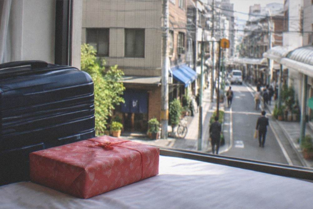 Wrapped mentaiko gift box beside a suitcase in a bright hotel room