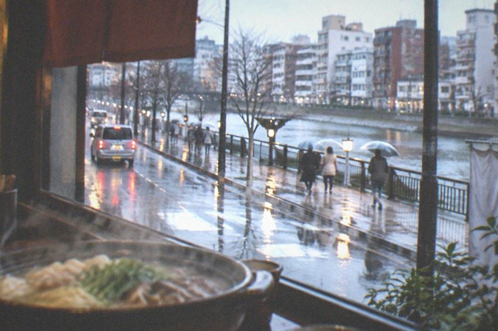 A hot pot steaming beside a rainy Fukuoka street seen through a restaurant window