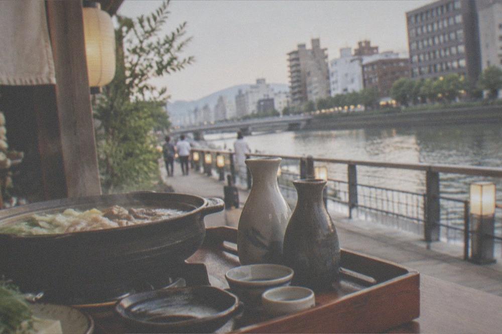 A wooden restaurant tray holding sake bottles and small drinking cups beside a hot pot
