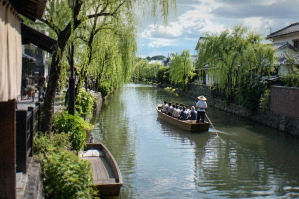 A flat pleasure boat gliding along a tree-lined canal in Yanagawa