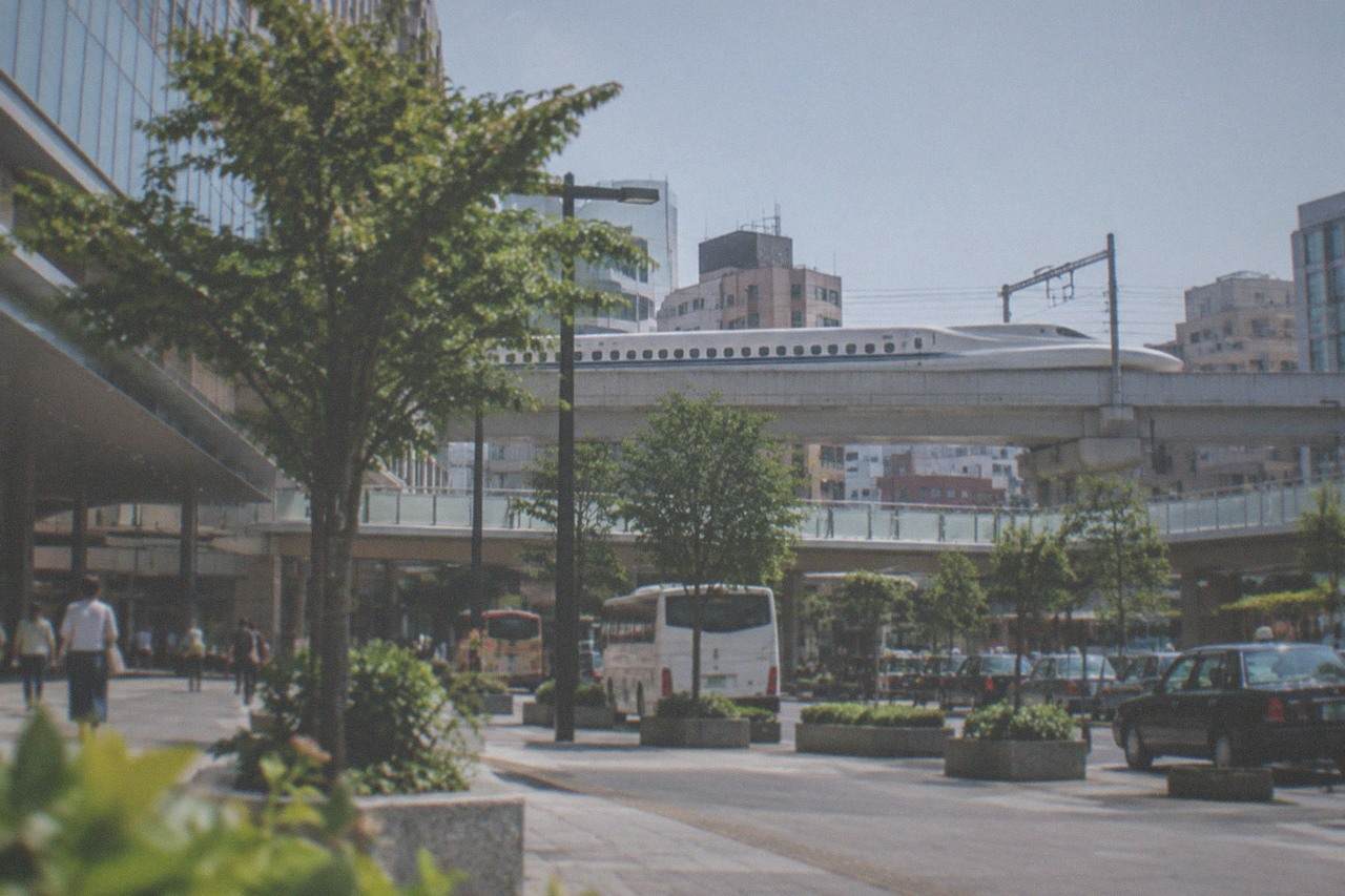 A sleek bullet train on an elevated track passing city buildings under a clear sky