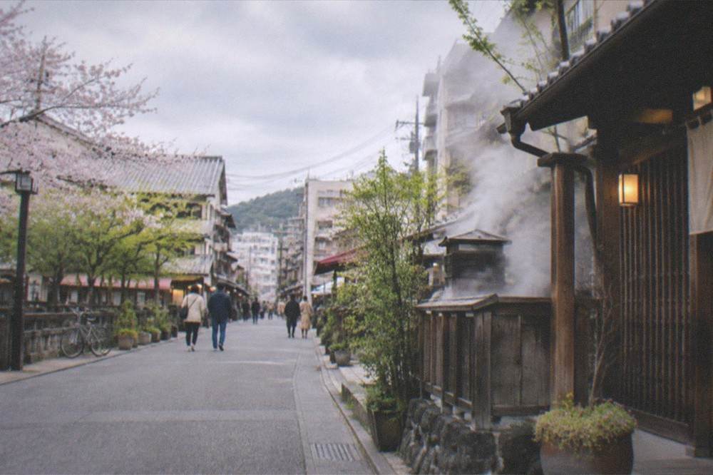 A hot spring town street with steam rising from vents beside wooden buildings