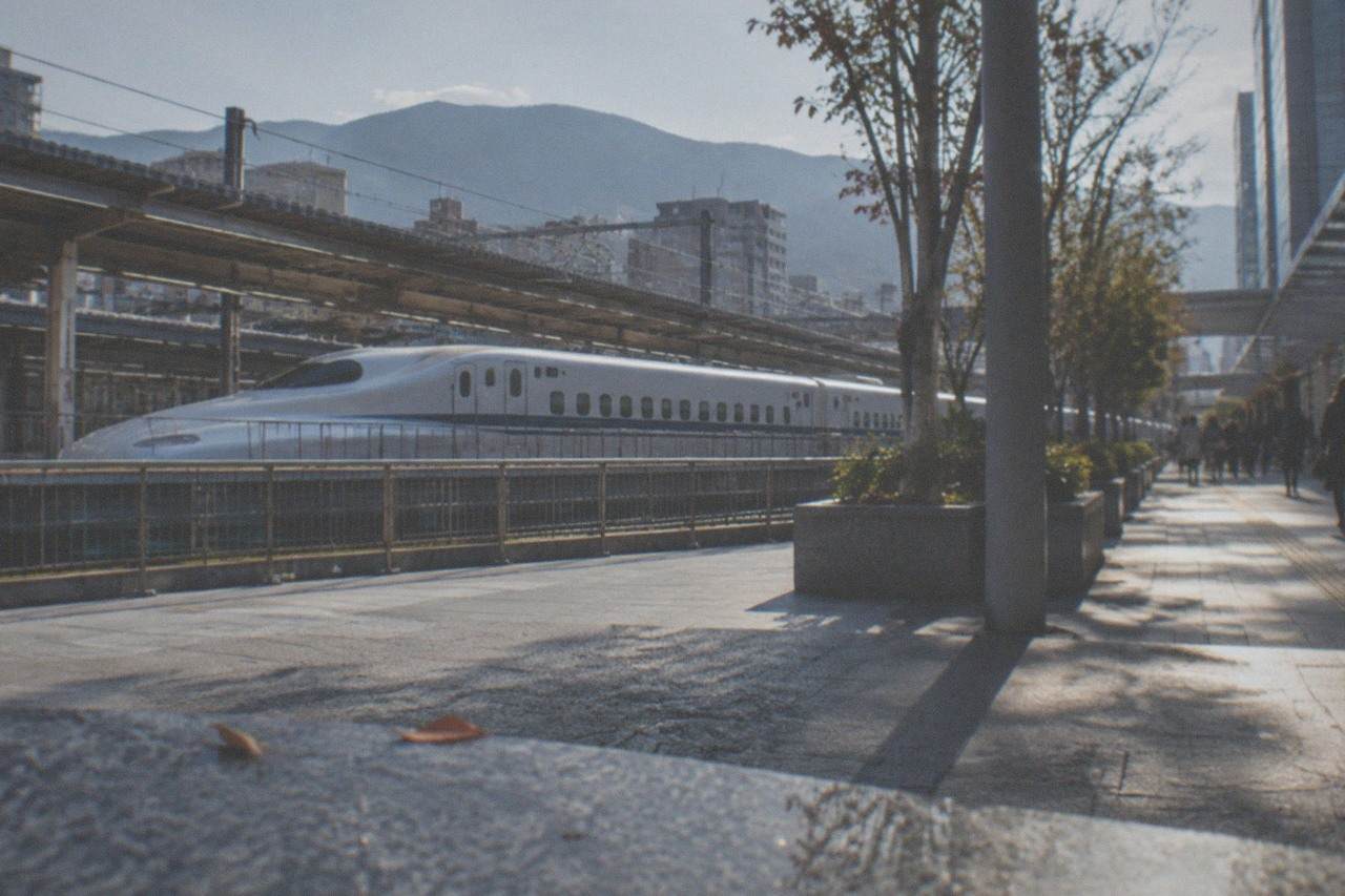 Shinkansen train at a station platform in Kyushu with mountains in the distance