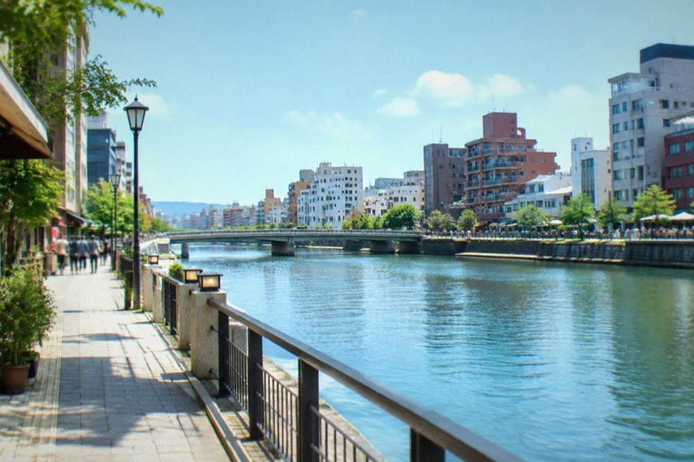 Neon signs reflecting on the Naka River alongside riverside food stalls in Nakasu
