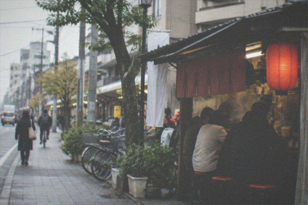 Customers seated side by side on stools at a narrow food stall counter