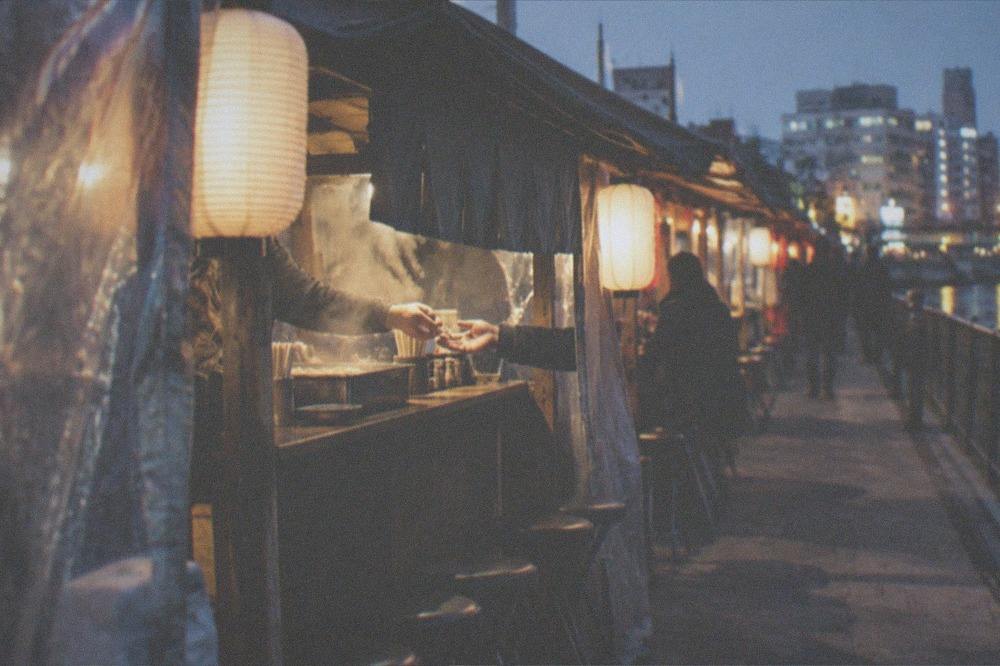 A hand passing coins to a stall owner at a lit food stall counter at night
