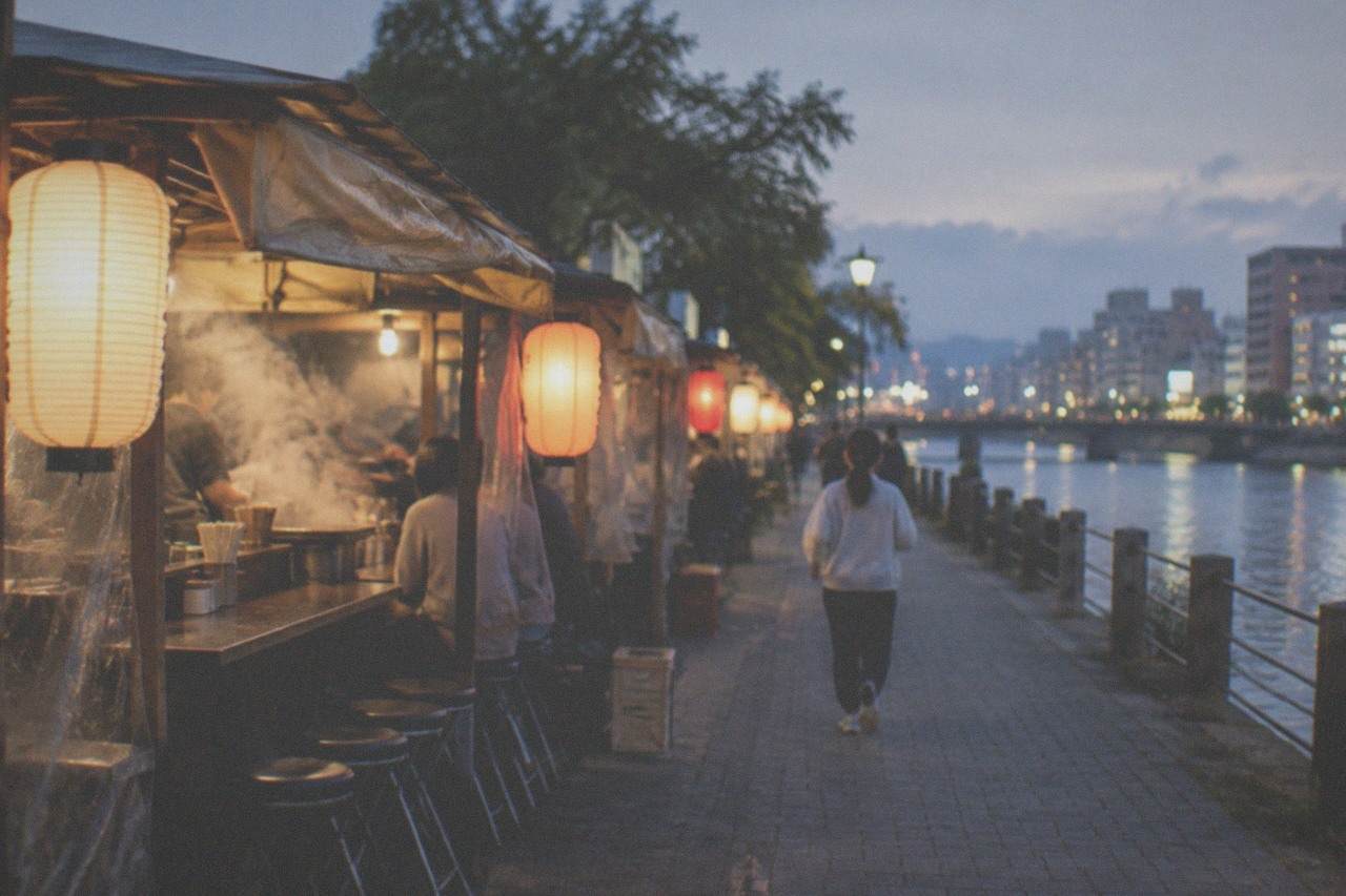 A row of illuminated food stalls lined up along a riverfront promenade at night