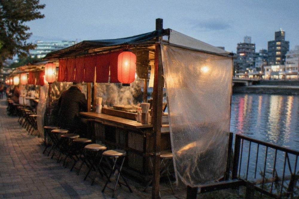 Red lanterns glowing above a yatai food stall beside the Naka River at night