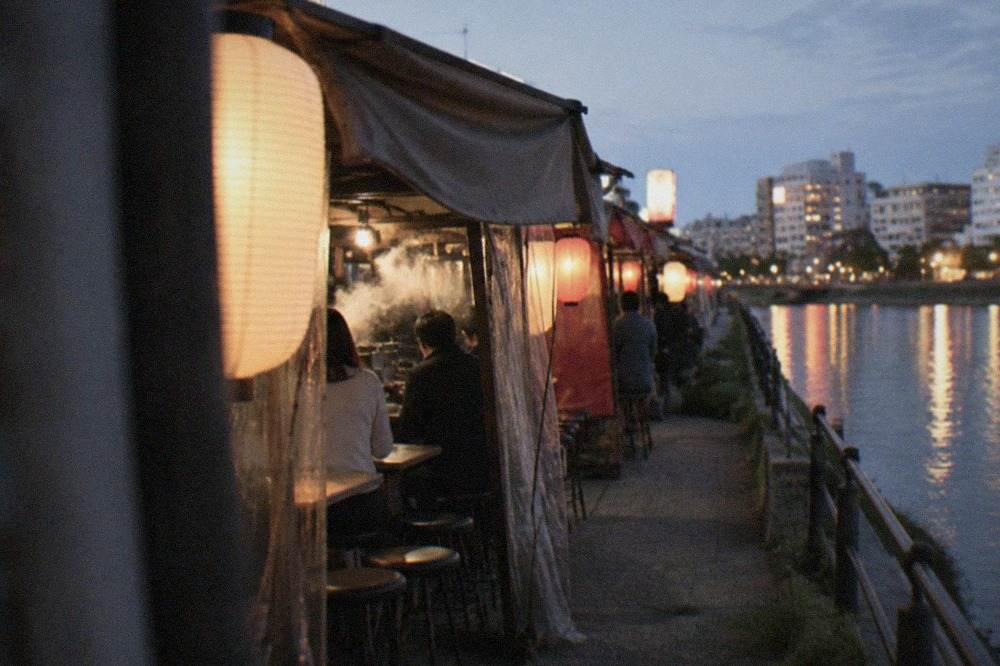 Evening lantern light reflecting on the Naka River beside rows of yatai food stalls in Nakasu