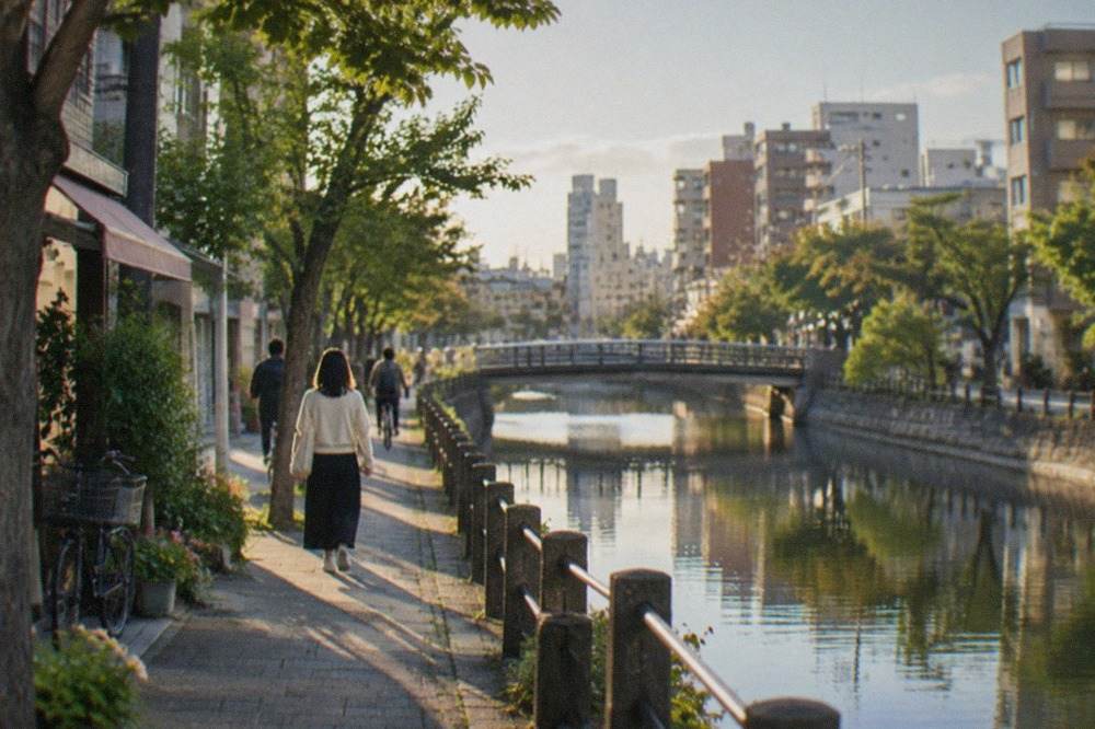 A quiet canal-side path in Fukuoka with trees reflected in the water on a clear morning